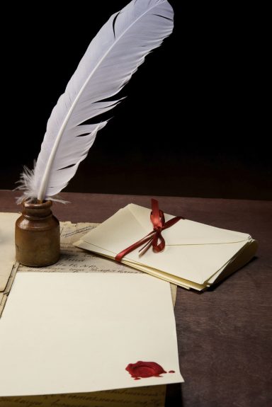 Pluma blanca, tintero y cartas con un sello de cera sobre una mesa.