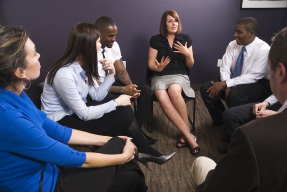 Familia de seis personas en una reunión, escuchando a una psicóloga que está hablando.