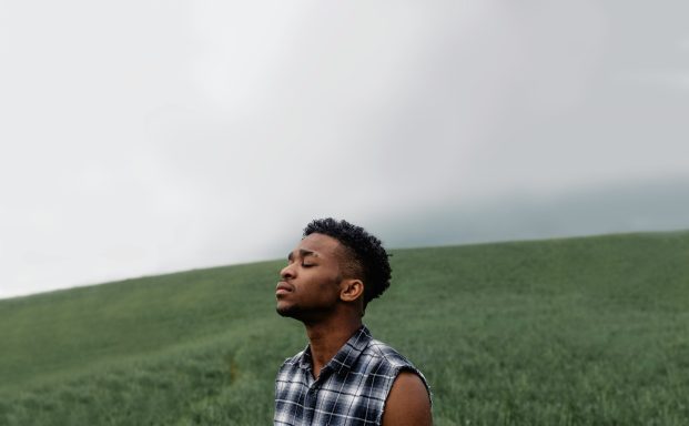 Hombre de pie en un campo, mirando al cielo con expresión contemplativa.